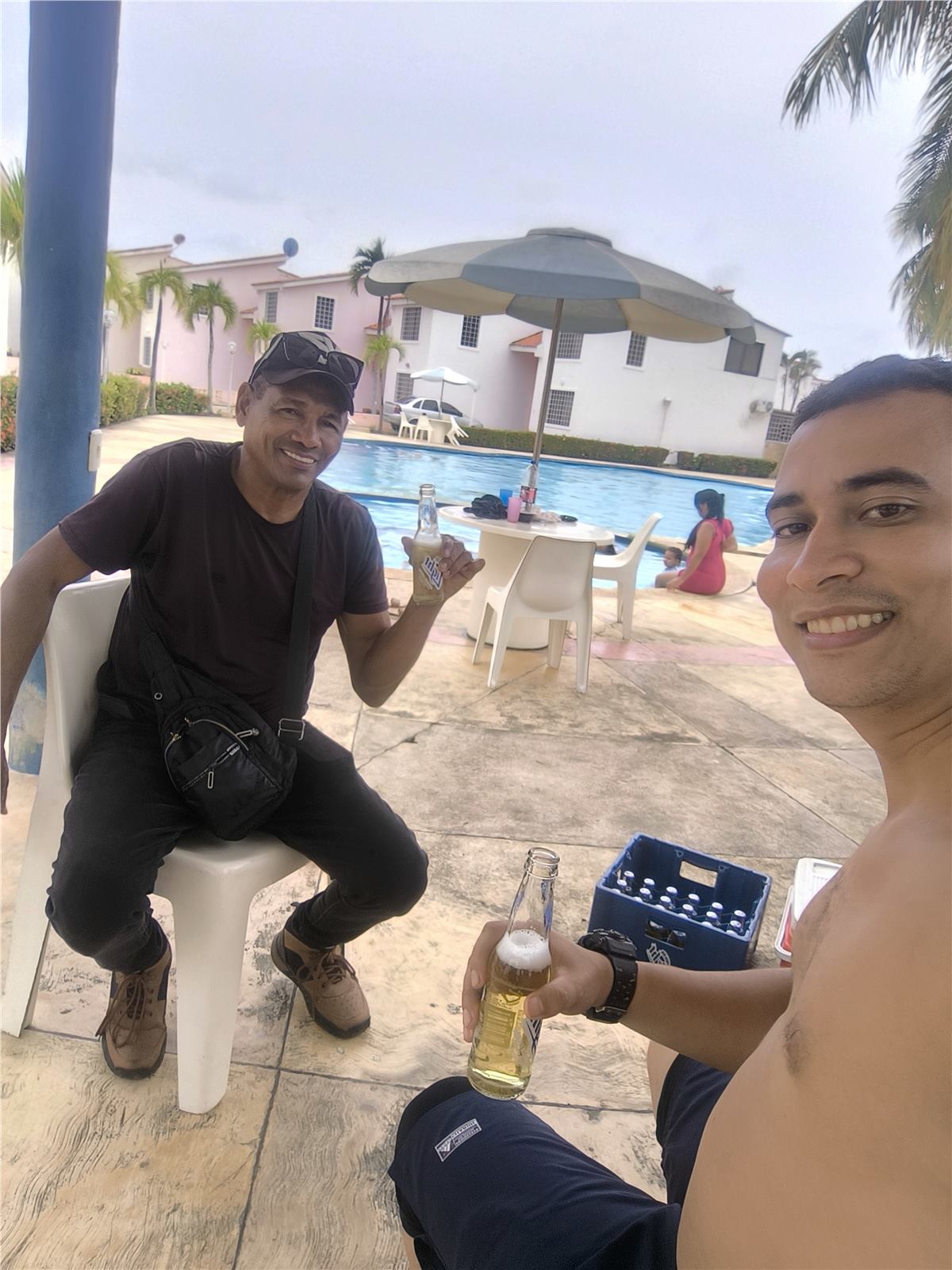 Personas descansando junto a la piscina con sombrilla y mesas